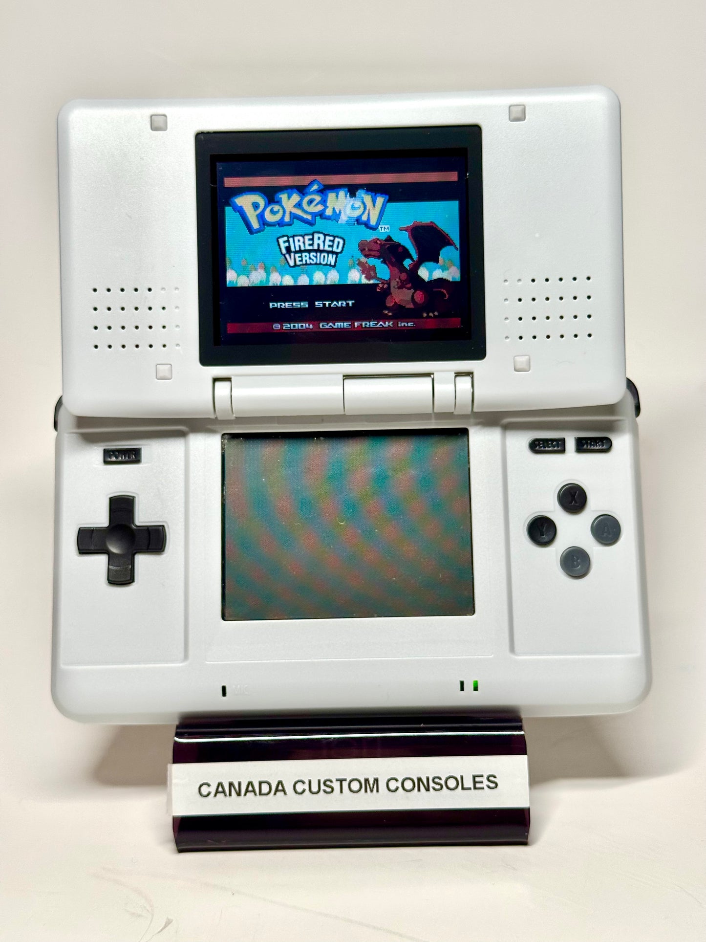 A Nintendo DS – SNES Edition displays the Pokémon FireRed Version start screen on a stand labeled CANADA CUSTOM CONSOLES, set against a plain white background—an ideal piece for retro gaming fans.