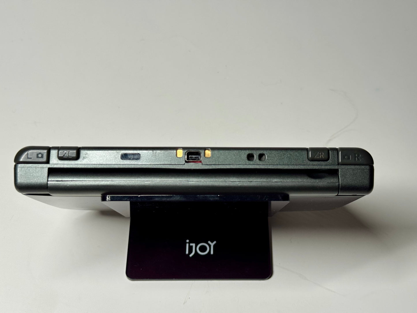A close-up of the top edge of a closed Nintendo Switch Lite — SNES Edition Custom Shell | 128GB, showing buttons, ports, and indicator lights as it rests on a black iJoy stand—ideal for fans of retro Nintendo designs.