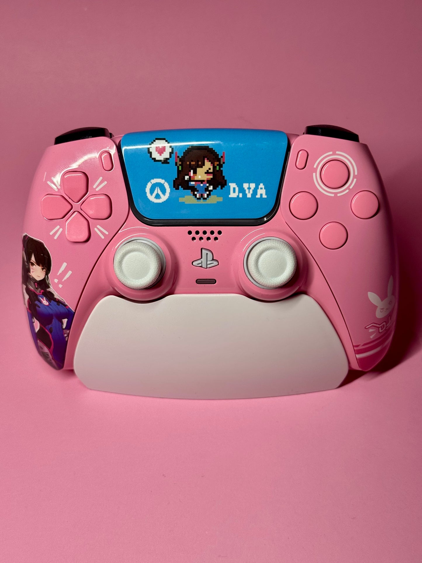 The D.Va Overwatch Custom PS5 Controller in pink features Hall Effect sticks, D.Va artwork and stickers, plus a pixel art D.Va graphic on the touchpad—all set against a matching pink background.