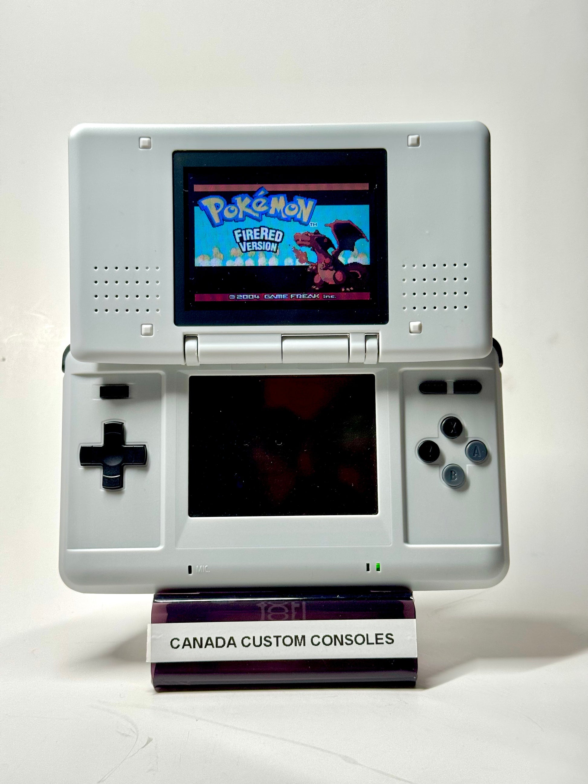 A Nintendo DS – SNES Edition displays the Pokémon FireRed Version title screen on a stand labeled CANADA CUSTOM CONSOLES, set against a plain white background—a unique find for retro gaming fans.
