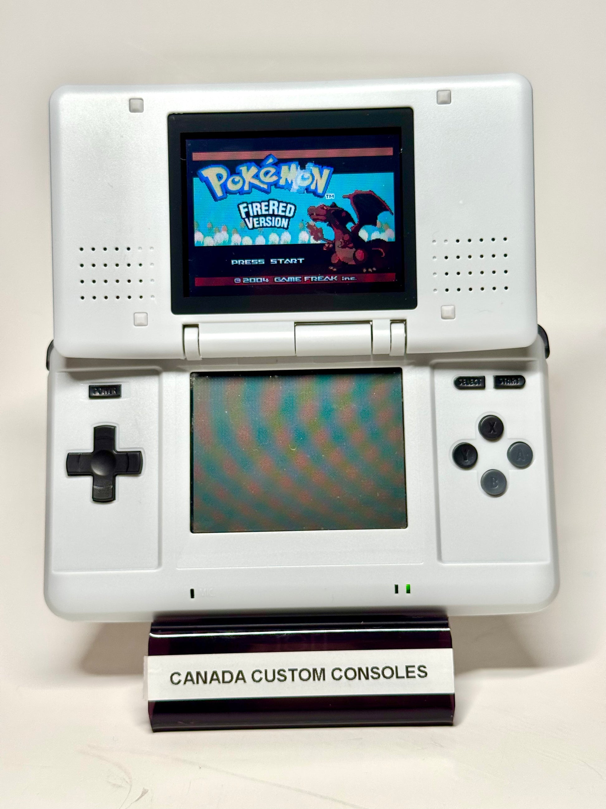 A Nintendo DS – SNES Edition displays the Pokémon FireRed Version start screen on a stand labeled CANADA CUSTOM CONSOLES, set against a plain white background—an ideal piece for retro gaming fans.
