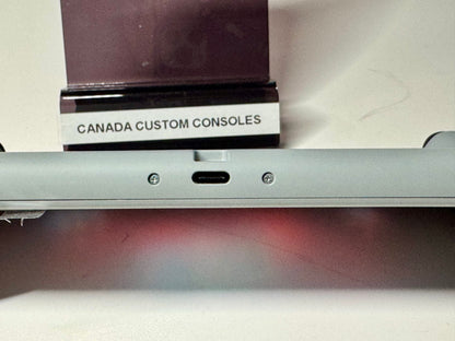 Close-up of a grey Nintendo Switch Lite — SNES Edition Custom Shell (128GB) showing its USB-C port and screws. In the background, a stand displays a CANADA CUSTOM CONSOLES label.