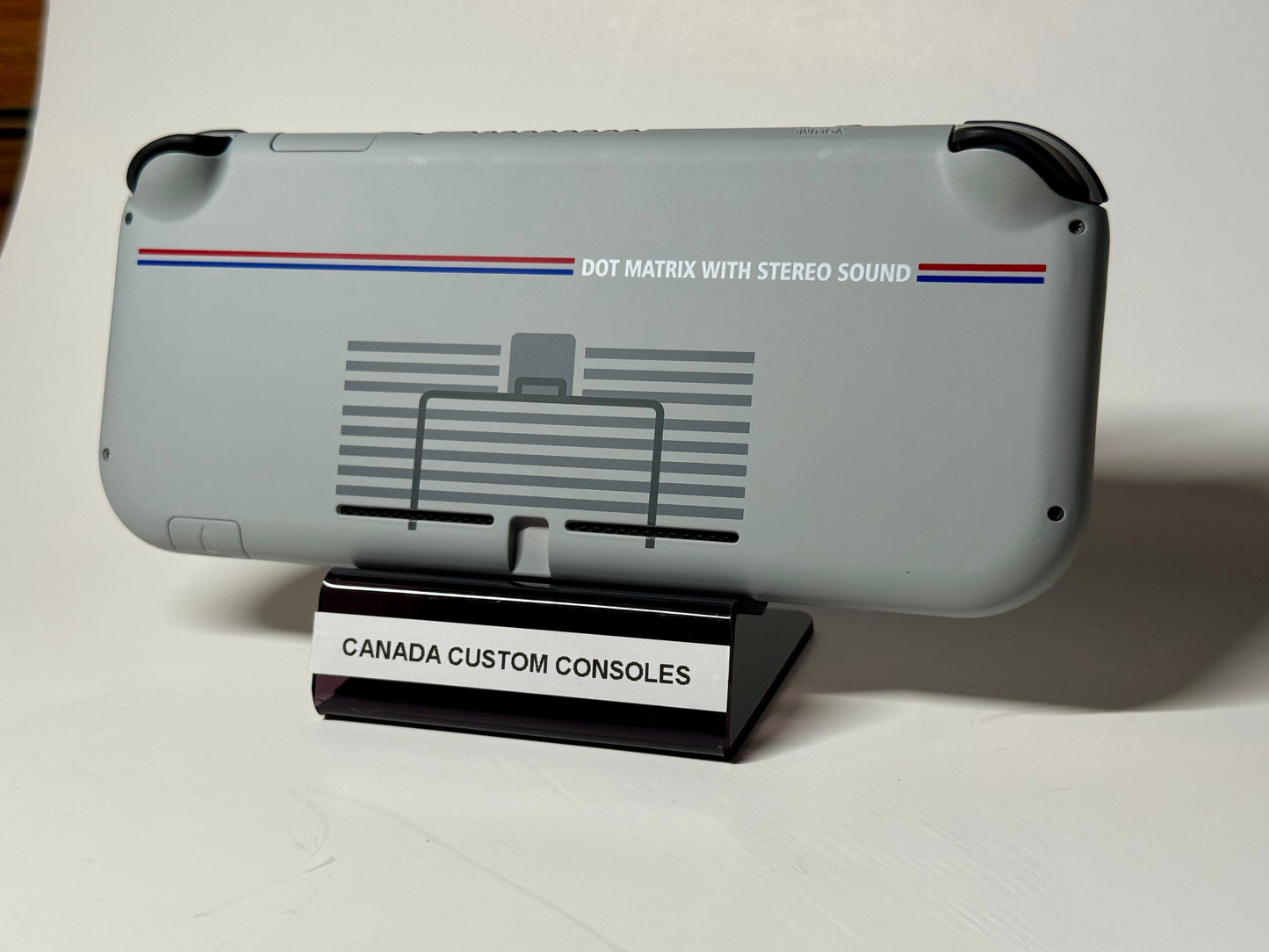 The Nintendo Switch Lite — SNES Edition Custom Shell | 128GB features a gray retro design with “DOT MATRIX WITH STEREO SOUND” on the back, displayed on a stand marked “CANADA CUSTOM CONSOLES,” and accented with nostalgic blue and red lines.