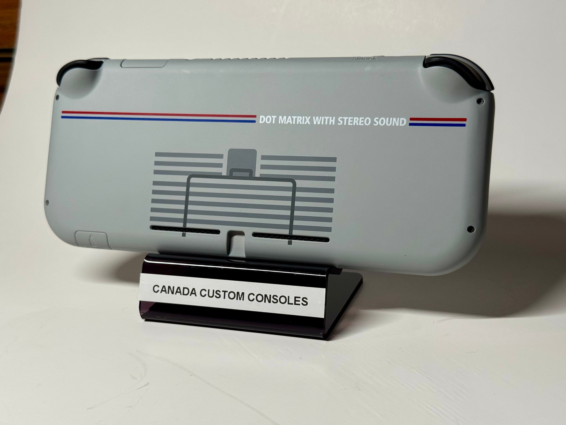 The Nintendo Switch Lite — SNES Edition Custom Shell | 128GB features a gray retro design with “DOT MATRIX WITH STEREO SOUND” on the back, displayed on a stand marked “CANADA CUSTOM CONSOLES,” and accented with nostalgic blue and red lines.