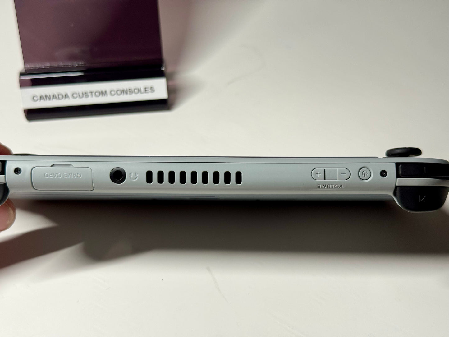 A close-up of the Nintendo Switch Lite — SNES Edition Custom Shell | 128GB displays its game card slot, cooling vents, headphone jack, and volume buttons. In the background, a CANADA CUSTOM CONSOLES stand highlights this retro handheld.