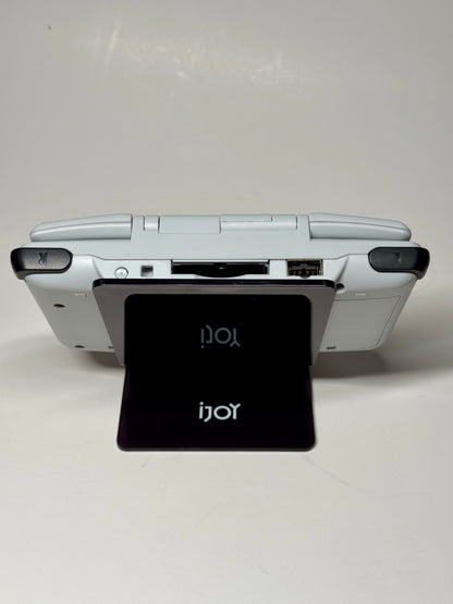 The Nintendo DS – SNES Edition, a white handheld in an SNES-style shell, is displayed on a black iJoy card stand. Viewed from the back, its cartridge slot and shoulder buttons evoke retro gaming nostalgia.