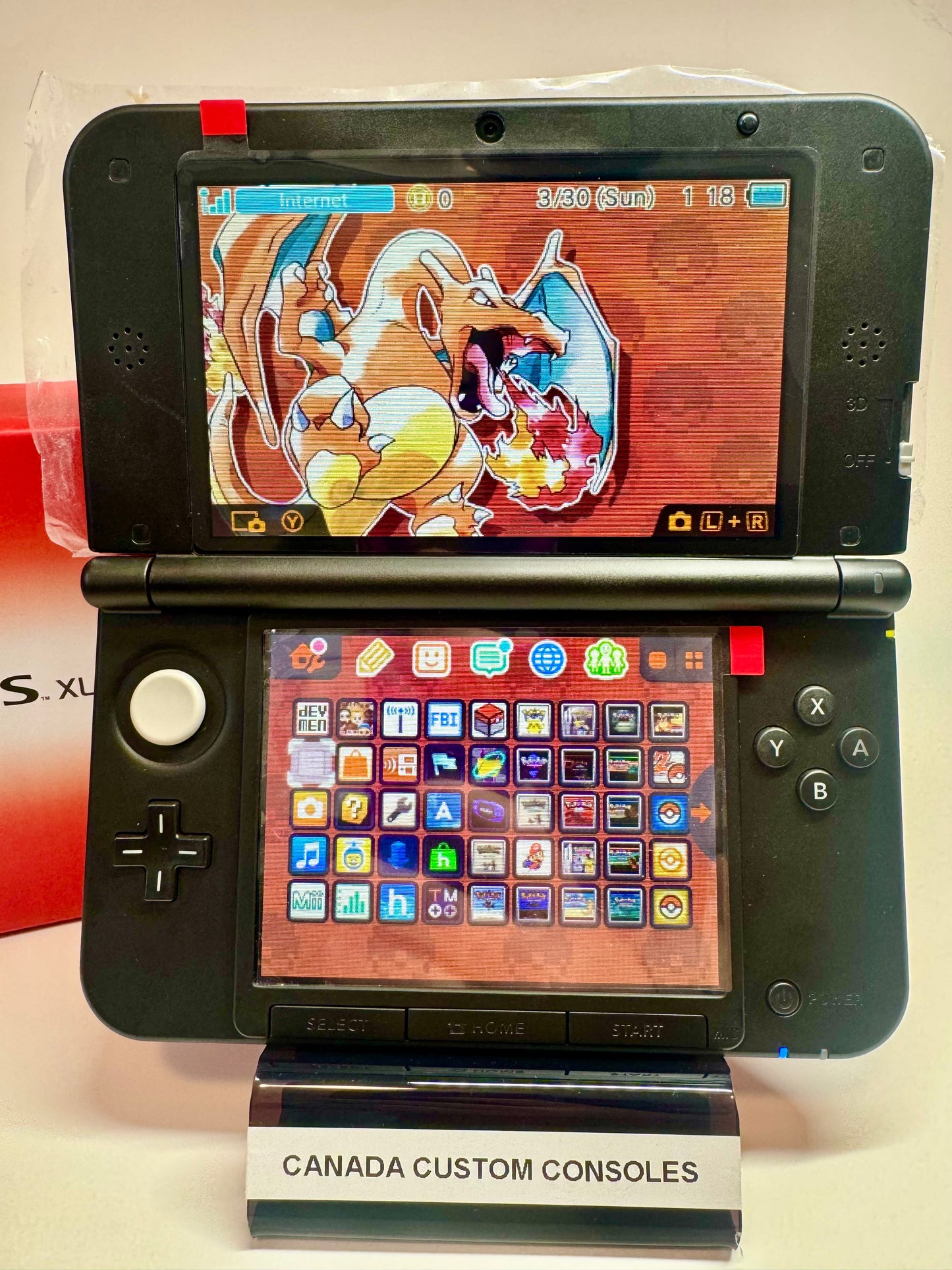 A red/black refurbished Nintendo 3DS XL—fully modded—features a Charizard-themed top screen, a colorful app icon grid, and sits on a stand labeled CANADA CUSTOM CONSOLES.