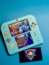 A Nintendo 2DS — Pokémon Sun & Moon Edition with a Pikachu decal shows the game on its top screen. A Canada Custom Consoles business card rests below, all set on a blue background. This system is region-free.
