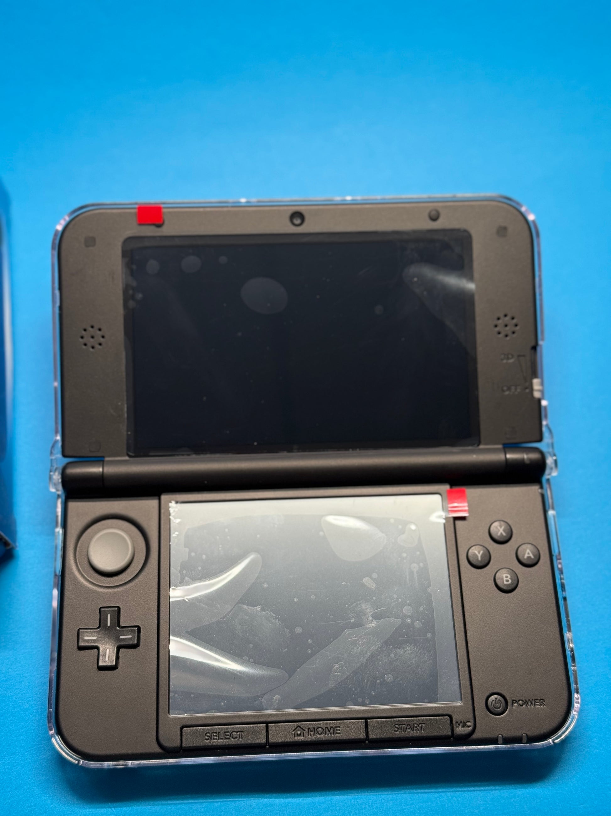 A fully modded Nintendo 3DS XL — Blue/Black handheld gaming console is open on a blue surface with protective plastic on both screens and two red stickers on the top screen’s corners.