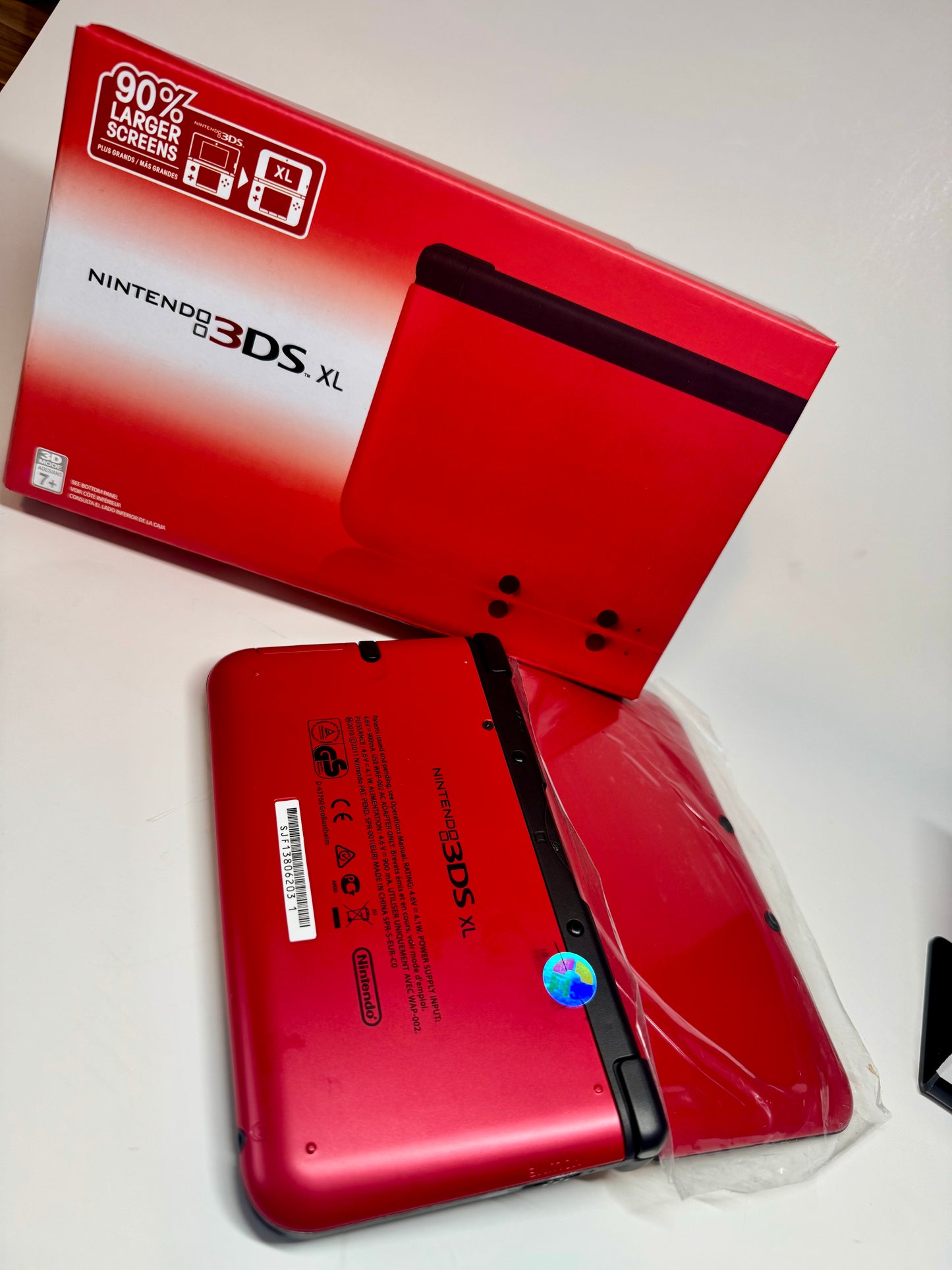 A refurbished Nintendo 3DS XL — Red/Black (fully modded) lies face down in a plastic sleeve beside its matching branded box, highlighting this collectible retro handheld console.
