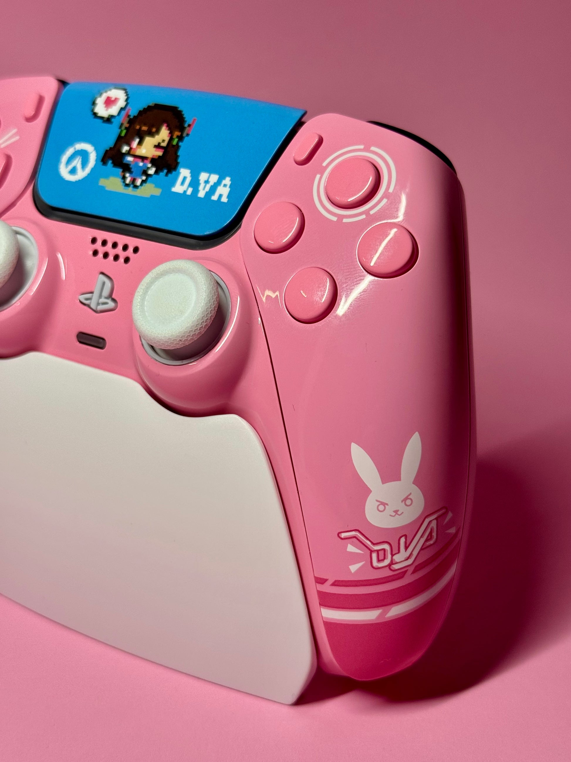 The D.Va Overwatch Custom PS5 Controller with Hall Effect Sticks in pink features a bunny logo and white accents, shown on a pink surface with an 8-bit D.Va on screen—perfect for Overwatch fans.