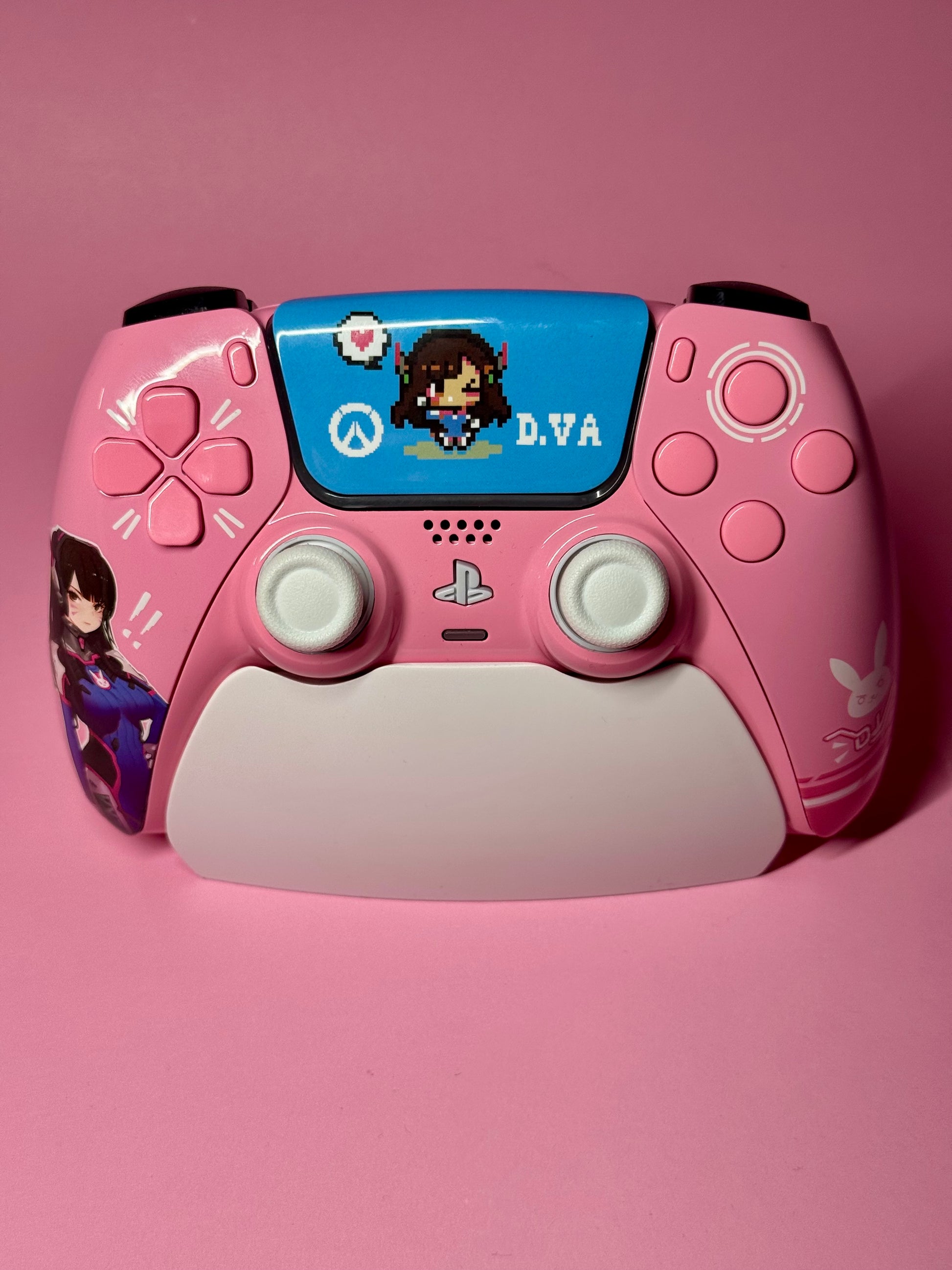 The D.Va Overwatch Custom PS5 Controller in pink features Hall Effect sticks, D.Va artwork and stickers, plus a pixel art D.Va graphic on the touchpad—all set against a matching pink background.