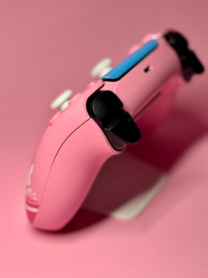 A D.Va Overwatch Custom PS5 Controller in pink, featuring Hall Effect sticks and white and black buttons, is displayed on a matching pink background.
