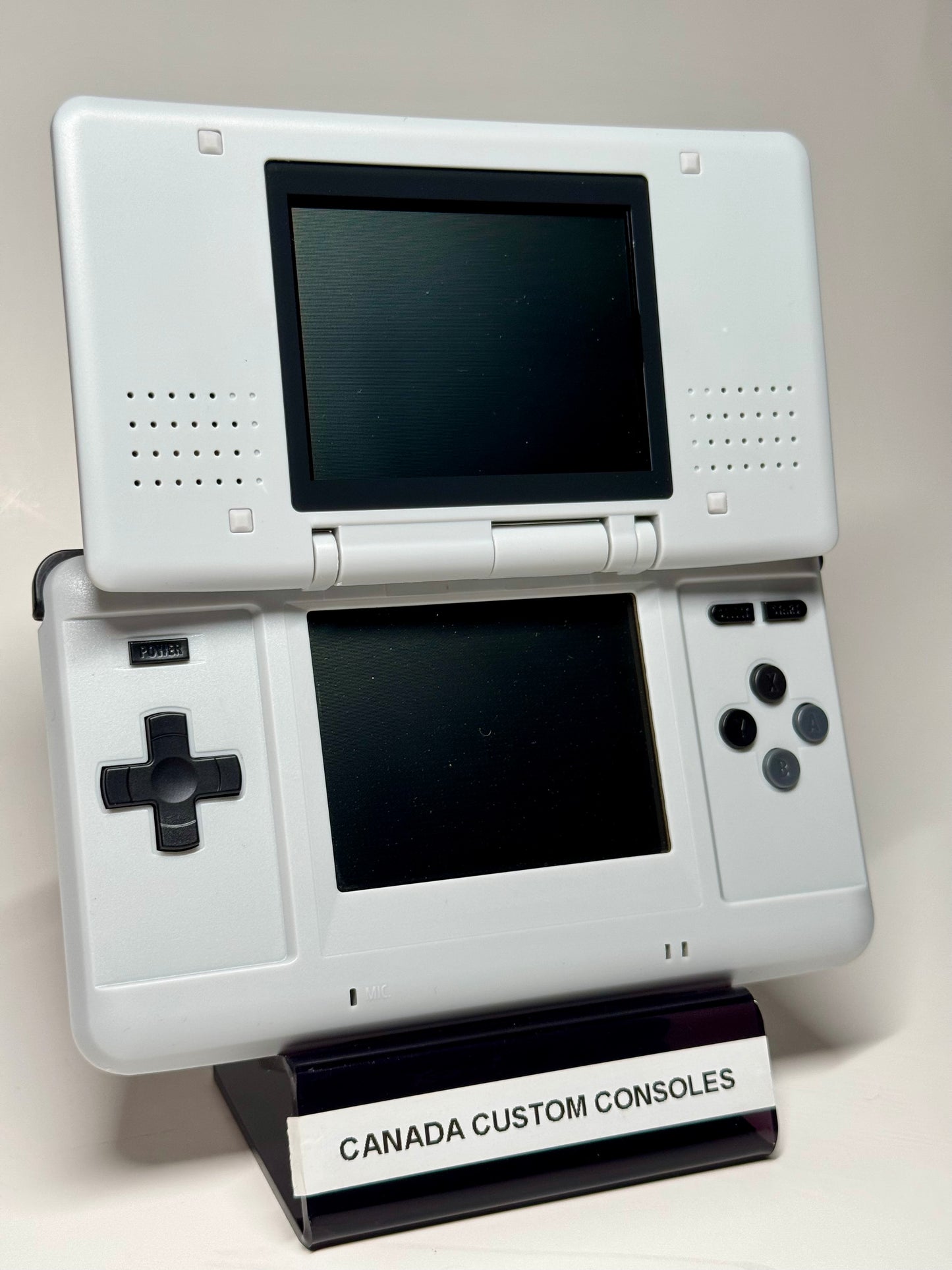 A Nintendo DS – SNES Edition handheld console is shown open on a stand labeled CANADA CUSTOM CONSOLES. Ideal for retro gaming, it features classic dual screens and standard controls.
