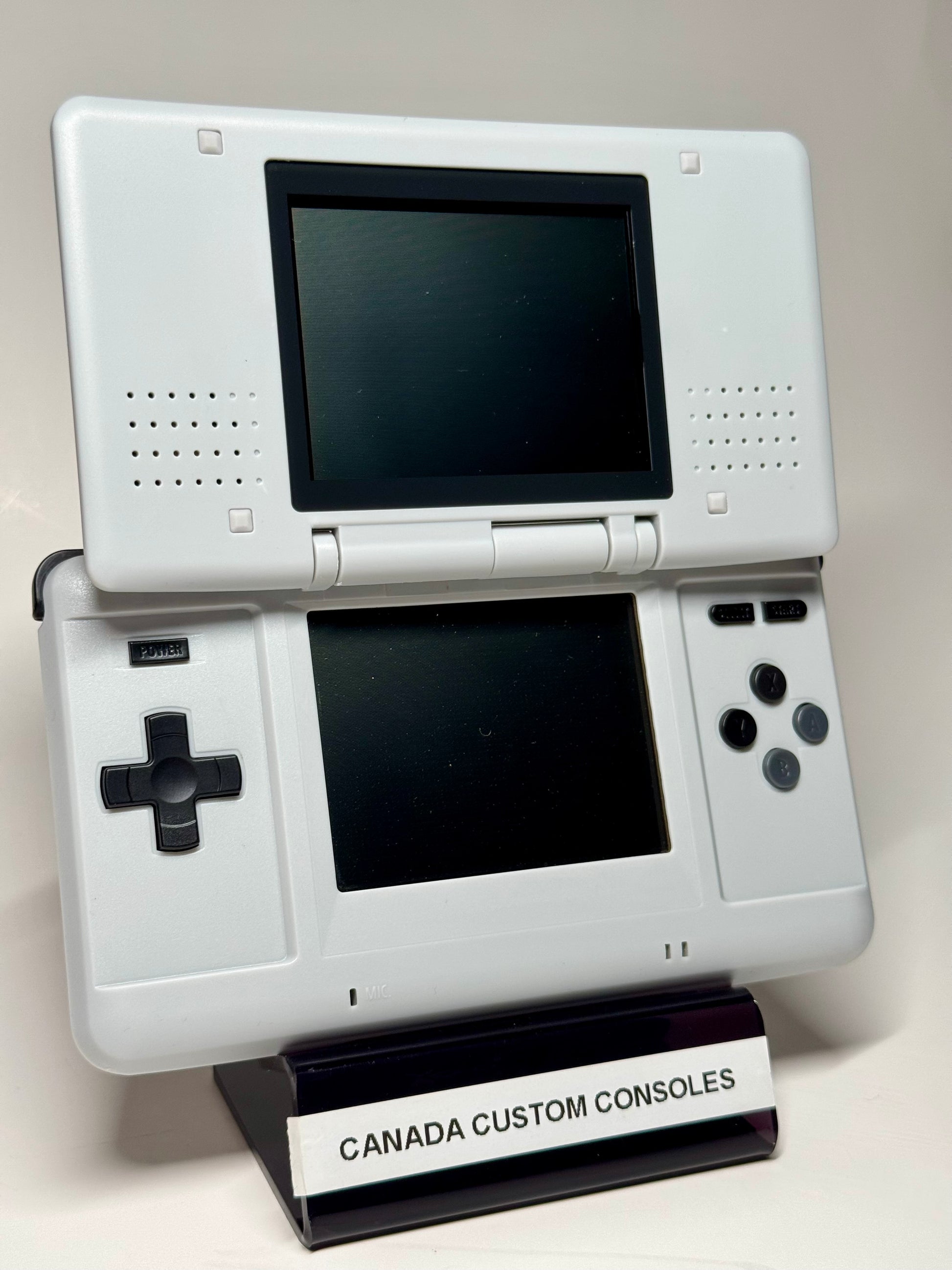 A Nintendo DS – SNES Edition handheld console is shown open on a stand labeled CANADA CUSTOM CONSOLES. Ideal for retro gaming, it features classic dual screens and standard controls.