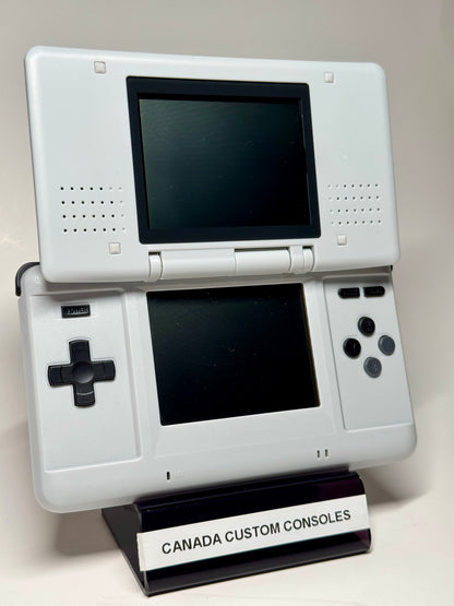 A Nintendo DS – SNES Edition handheld console is shown open on a stand labeled CANADA CUSTOM CONSOLES. Ideal for retro gaming, it features classic dual screens and standard controls.