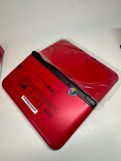 A refurbished red/black Nintendo 3DS XL — fully modded — rests face down on a white surface, partly wrapped in clear plastic with visible labels and logos on the back.