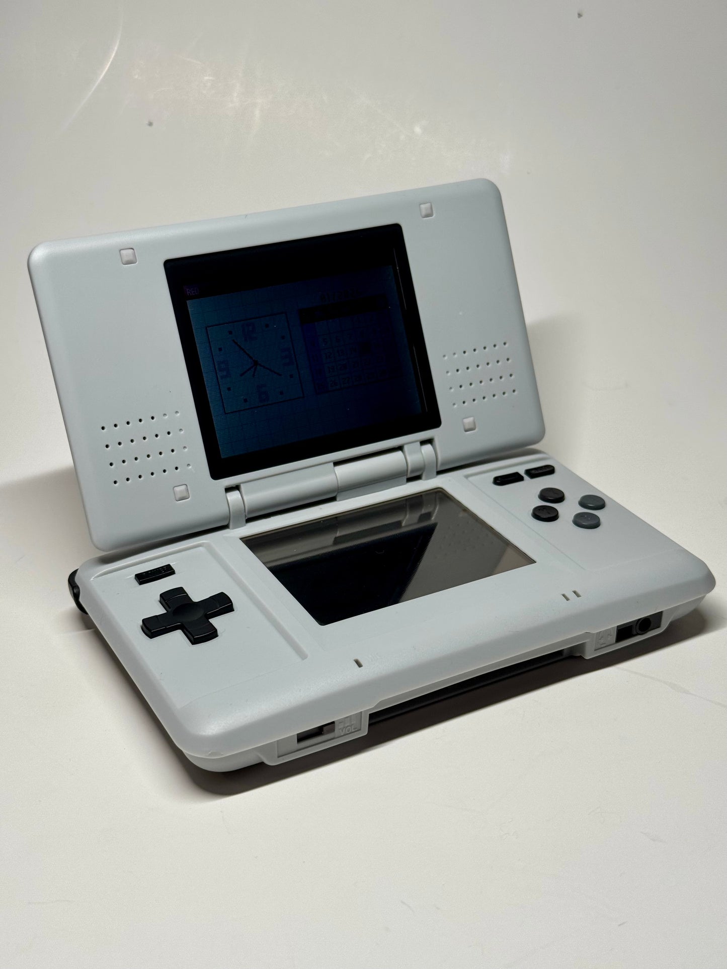 A Nintendo DS – SNES Edition handheld console is open, showcasing gameplay on its upper screen. Featuring a directional pad, buttons, and dual screens, it’s ideal for retro gaming against a plain white background.