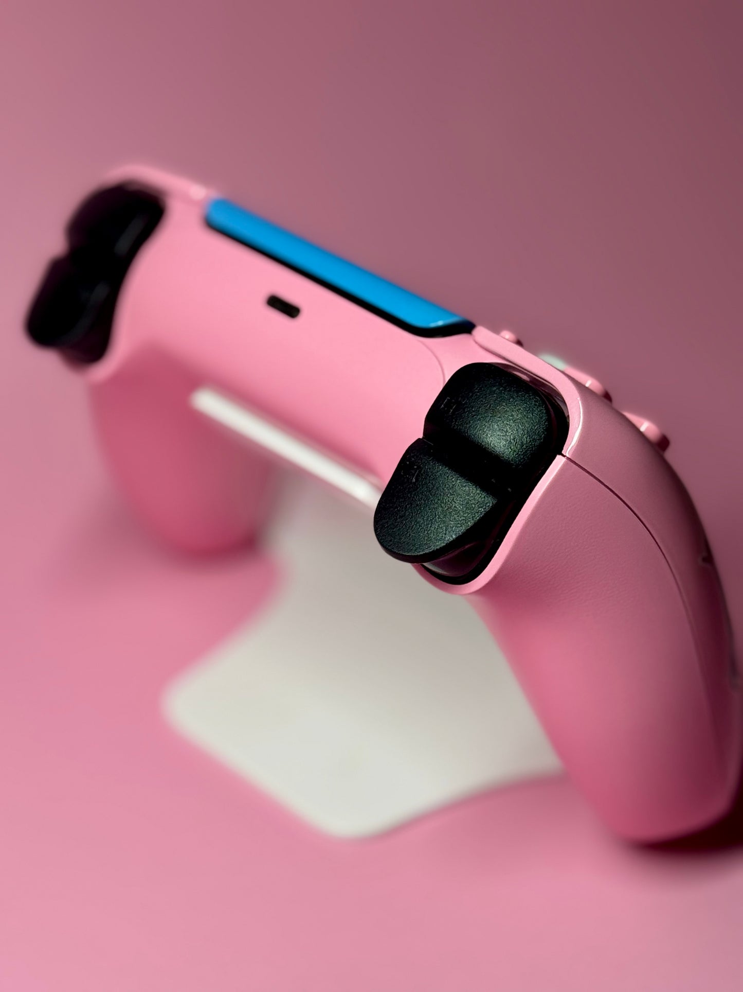 A D.Va Overwatch Custom PS5 Controller with Hall Effect sticks, finished in pink with blue accents, rests on a white stand against a pink background.