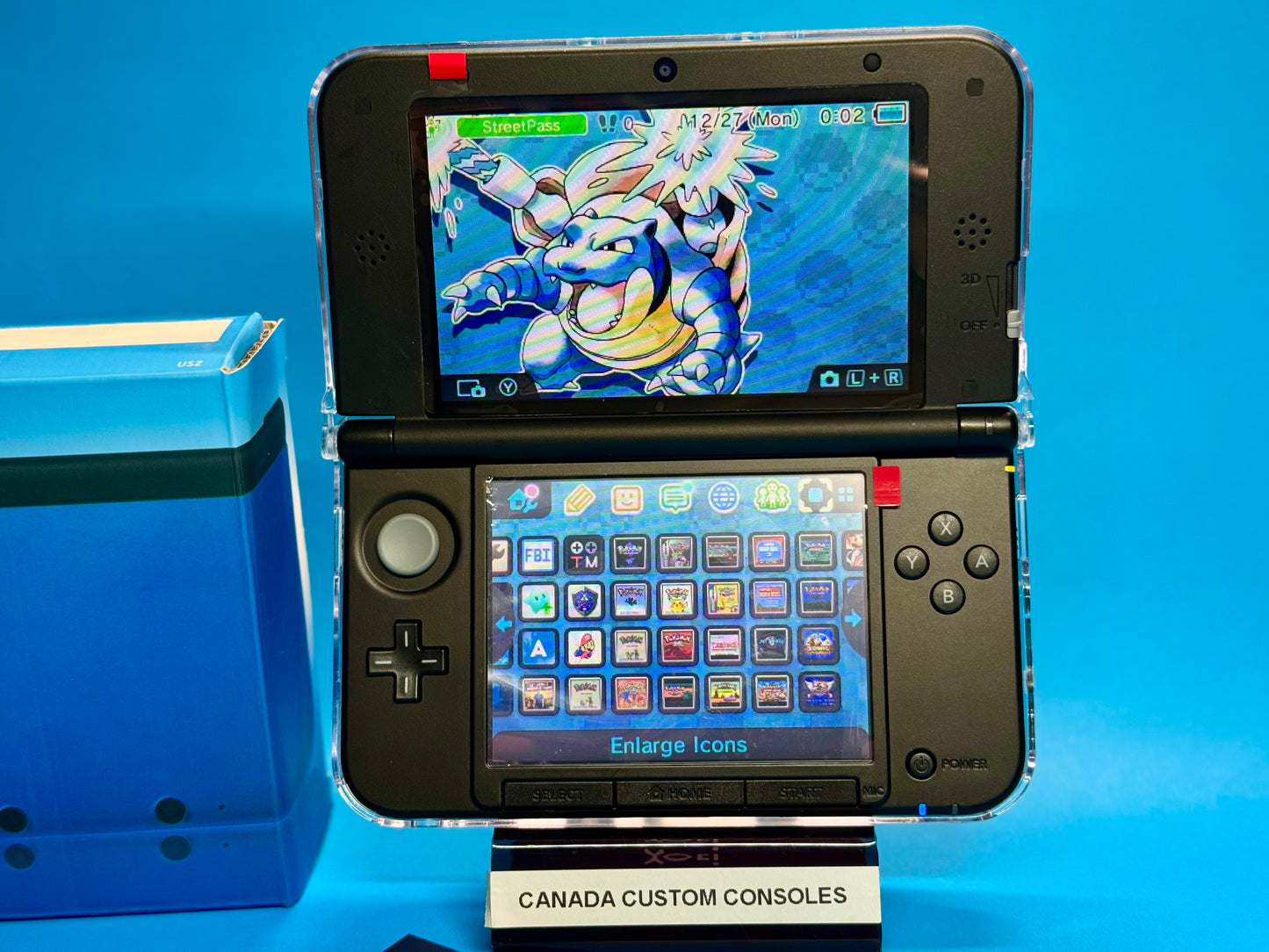 A fully modded Nintendo 3DS XL — Blue/Black features a custom transparent shell, Blastoise theme on the top screen, pre-installed games, and app icons below. Labeled CANADA CUSTOM CONSOLES, it sits beside a blue box.