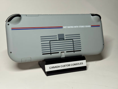 The Nintendo Switch Lite — SNES Edition Custom Shell | 128GB features a retro design with stripes, nostalgic graphics, and “DOT MATRIX WITH STEREO SOUND” text. It comes gray, handheld, resting on a stand labeled “CANADA CUSTOM CONSOLES.”.