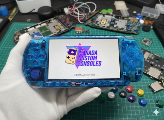 A gloved hand holds a Modded Sony PSP 3000 with a custom blue shell, running CFW and games, shown on a Canada Custom Consoles screen amid disassembled electronics and parts on a green cutting mat.