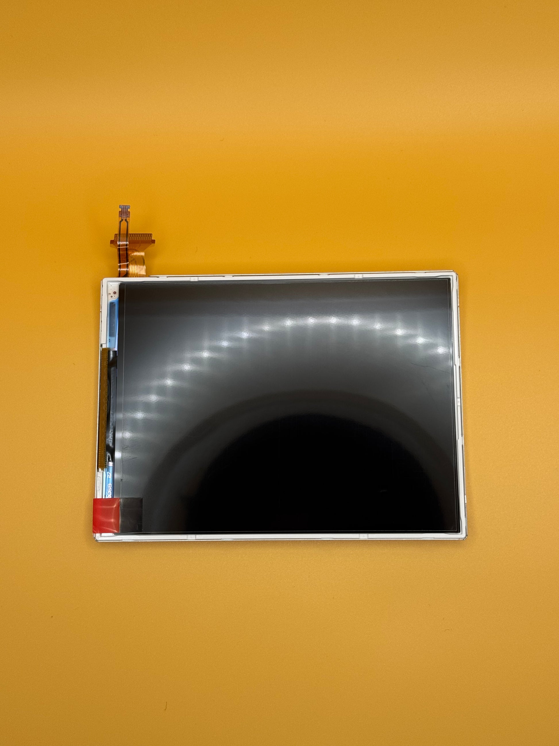 The NEW Nintendo 3DS XL/LL Lower Screen Replacement, featuring a black surface and visible connectors, is shown on a solid orange background—ideal for replacing the lower screen of your device.