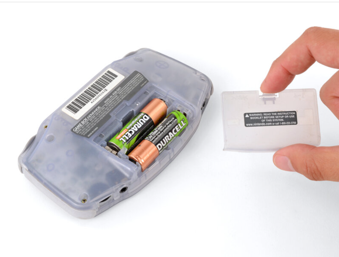 A hand removes the battery cover from a Game Boy Advance –Gengar Edition | IPS 3.0 Laminated Display | Custom Build, revealing two AA Duracell batteries inside the compartment.