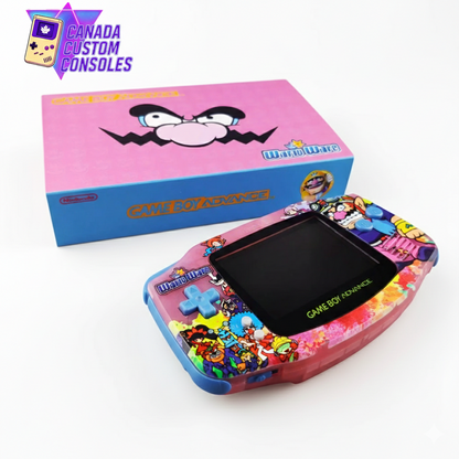 The Game Boy Advance – Wario Edition | IPS 3.0 Laminated Display | Custom Build features vibrant WarioWare-themed art and is displayed before a pink box with Wario’s face and the Canada Custom Consoles logo in the top left corner.